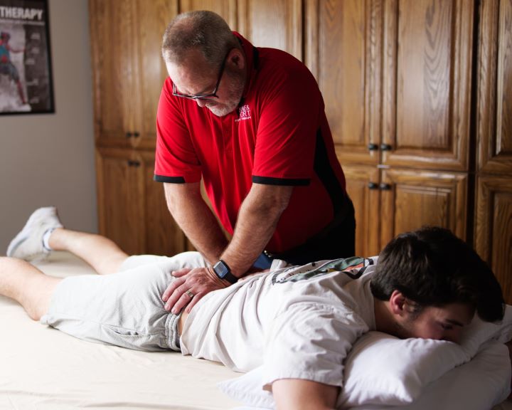 a provider applying a therapy technique to a patient's low back as the patient lies on their stomach on a treatment table